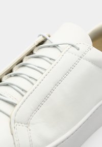 Chaussure en cuir blanc avec une finition lisse, dotée de lacets gris clair et de coutures détaillées sur la tige. Design à bout rond.