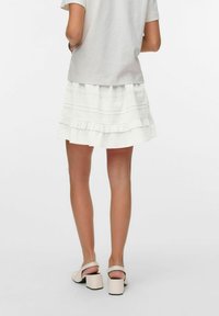 Falda blanca con volantes de capas, fabricada con tejido texturizado y adornos de encaje decorativo, combinada con una blusa de color claro y sandalias de tacón.