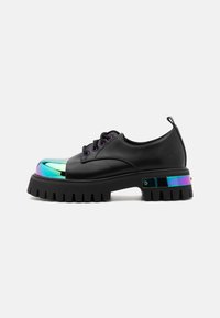 Sapatos de couro preto com uma sola robusta, biqueira iridescente e detalhes refletivos no calcanhar. Apresenta ilhós e atacadores roxos.