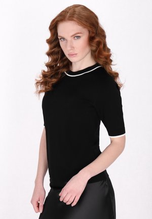 Pulover scurt negru cu mânecă scurtă și garnitură albă la decolteu și mâneci, fabricat dintr-un material fin, cu un design ajustat și guler tip cerc.