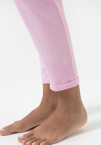 Lichtroze cropped broeken gemaakt van zachte stof, met opgerolde mouwen, met blote voeten zichtbaar eronder en een gladde, egale textuur.