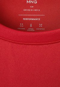 Étiquette en tissu rouge indiquant MNG slim fit, taille M, avec des icônes et du texte pour une performance fonctionnelle, thermorégulatrice et confortable.