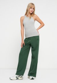 Sivý rebrovaný top s ramienkami spárovaný s voľnými zelenými teplákmi. Outfit dopĺňajú biele tenisky so zelenými akcentmi.