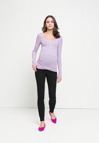 Duga, svijetlopurple prugasta majica s dugim rukavima i detaljima od dugmadi, u kombinaciji s crnim uskim hlačama i svijetloružičastim balerinkama. Glatka tekstura tkanine.