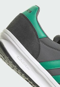 Chaussure de sport grise avec un accent en cuir vert, texture en daim, et une semelle intermédiaire Cloudfoam blanche avec une semelle extérieure noire texturée.