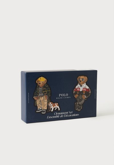 Boîte Polo Ralph Lauren bleu marine avec deux ornements ours habillés de vêtements décontractés et sportifs, et un petit chien à côté d’un des ours.