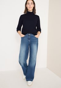 Granatowy sweter z golfem w połączeniu z jasnoniebieskimi, szerokimi spodniami. Spodnie mają wysoki stan oraz kieszenie z przodu. Uzupełnione białymi trampkami.