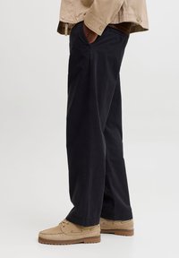 Μαύρο παντελόνι με φαρδιά πόδια από βαμβάκι, με πλευρικές τσέπες, άνετη εφαρμογή και ρεβέρ στο τελείωμα. Συνδυάζεται με μπεζ παπούτσια μοκασίνια.