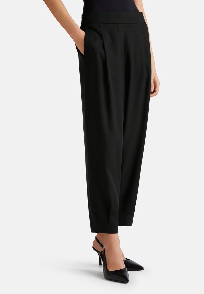 Svart skräddarsydda byxor med en slät textur, med sidofickor och veck, tillsammans med svarta klackskor för en extra sofistikerad look.