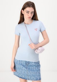 T-shirt azzurro fitted con un logo triangolare rosso, abbinato a una gonna in denim con un motivo a logo ripetuto, e una piccola borsa rosa.