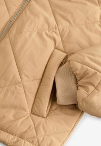 Giacca trapuntata beige chiaro con una texture liscia, caratterizzata da una chiusura con zip e dettagli a polsino lavorato a maglia.