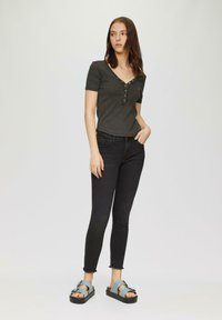 Donkergrijze blouse met korte mouwen, een V-hals en knoopaccenten, gecombineerd met zwarte aansluitende jeans en blauwe sandalen met een gedurfde bandontwerp.