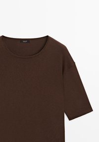 Haut marron en tricot à manches courtes avec encolure ronde et étiquette cousue visible à l'intérieur du col sur fond blanc.
