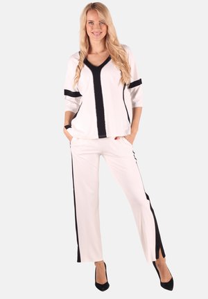 Weißes Zweiteiler-Outfit mit einem V-Ausschnittshirt mit schwarzen Akzenten und dreiviertellangen Ärmeln, kombiniert mit geraden Hosen mit seitlichen Schlitzen.