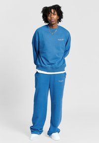 Niebieski bawełniany sweter i dopasowane spodnie o luźnym kroju. Posiada logo na klatce piersiowej i kieszeni, zestawione z białymi trampkami.