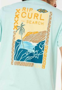 Himmelblaues Baumwoll-T-Shirt mit einem bunten Grafikdesign eines Palmenbaums, Ozeans und Bergen sowie dem Text "RIP CURL THE SEARCH."
