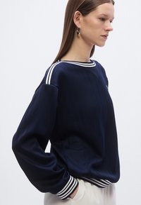 Pull côtelé bleu marine avec des détails de rayures blanches aux poignets et à l'encolure, présentant une coupe décontractée et une texture douce.