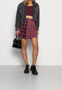 Černá krátká džínová bunda, vínový krátký top, kostkovaná minisukně v odstínech bordó. Doplňky zahrnují malou černou kabelku a lesklé černé boty.