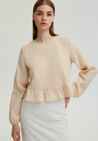 Beige blouse met lange mouwen, een ronde halslijn en een gerimpelde zoom. Gemaakt van lichte stof, met een comfortabele pasvorm en een minimale textuur.