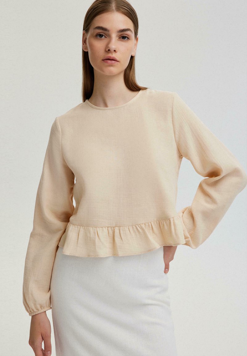 Beige blouse met lange mouwen, een ronde halslijn en een gerimpelde zoom. Gemaakt van lichte stof, met een comfortabele pasvorm en een minimale textuur.