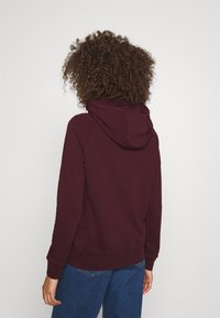 Burgundská mikina s kapucí vyrobená z měkké látky, s tkaničkou v kapuci, žebrovanými manžetami a spodním lemem, která má pohodlný střih a minimalistický design.