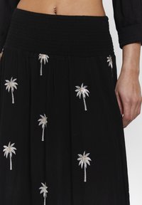 Svart kjol med resårmidja, prydd med silverfärgade palmer broderade över hela. Tillverkad av lätt, texturerad tyg.
