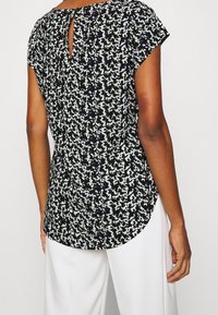 Haut à motifs noir et blanc avec manches courtes, ourlet arrondi, détail dos avec ouverture en forme de clé et tissu léger. Associé à un bas blanc.