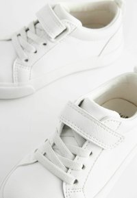 Hvide børnesneakers lavet af syntetisk læder med en glat tekstur, der har både snørebånd og en velcro-strop til lukning.