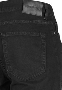 Mustat farkut nahka-bränditarralla, joissa on takatasku ja hienovaraiset ommeltyöt. Kangas on sileä.