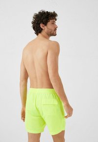 Bañador amarillo neón con cintura elástica y un bolsillo lateral. Los pantalones cortos son ligeros y de longitud media hasta el muslo en un color sólido.