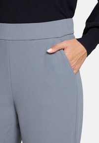 Pantalon gris avec une texture lisse, une large ceinture et une poche latérale. Le tissu a une légère brillance avec une coupe ajustée.