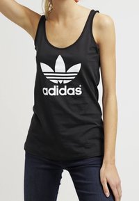 Svart linne i bomull med en stor vit Adidas-logotyp med trefoil-design. Slät textur och figurnära passform.