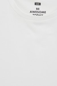 Fehér pamut póló kerek nyakkal, melynek gallérján fekete nyomtatott szöveg olvasható: "LÉGY KIVÁLÓ MA".