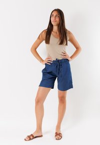 Pantalones cortos de algodón azul marino con cintura elástica y cordón, con bolsillos laterales y un ajuste relajado, combinados con una camiseta sin mangas beige.
