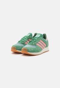 Green and pink sneakers with suede and mesh panels, featuring three pink stripes on the sides and a textured rubber sole.