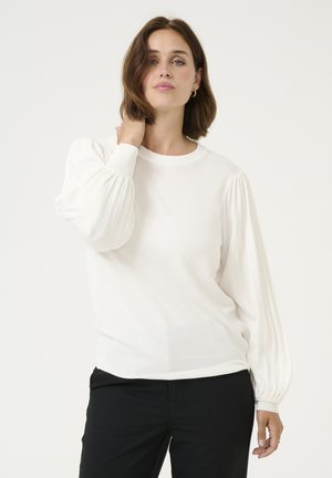 White sweater with ribbed puff sleeves, round neckline, and a soft texture. Paired with black pants, featuring a relaxed fit.