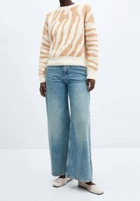 Suéter crema con rayas de cebra en tono melocotón, combinado con jeans de pierna ancha color azul claro y zapatos planos beige. Textura suave y ajuste relajado.