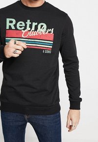 Schwarzer Pullover mit langen Ärmeln, mit einem bunten "Retro Clubbers"-Motiv und horizontalen Streifen in Rot und Blau.