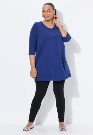 Marineblauwe tuniek met een V-hals en driekwartmouwen, gecombineerd met zwarte leggings en metallic platte schoenen. Gladde stof, relaxte pasvorm.