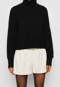 Zwart coltrui met een cropped ontwerp, gemaakt van een zachte stof. Voorzien van lange mouwen en geribbelde details bij de kraag.