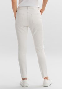 Vita smala jeans i denim, med bakfickor och en mjuk textur. Matchade med vita sneakers, visade från baksidan.