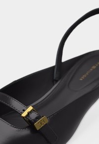 Μαύρο γυαλιστερό παπούτσι με λουράκι πίσω και χρυσή αγκράφα, με επένδυση στο πέλμα, κοντινή γωνιακή λήψη σε λευκό φόντο.