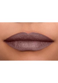 Matt läppstift i en dämpad mauve nyans, som framhäver glatta, fylliga läppar med en texturerad finish och subtila veck, mot en mjuk hudbakgrund.