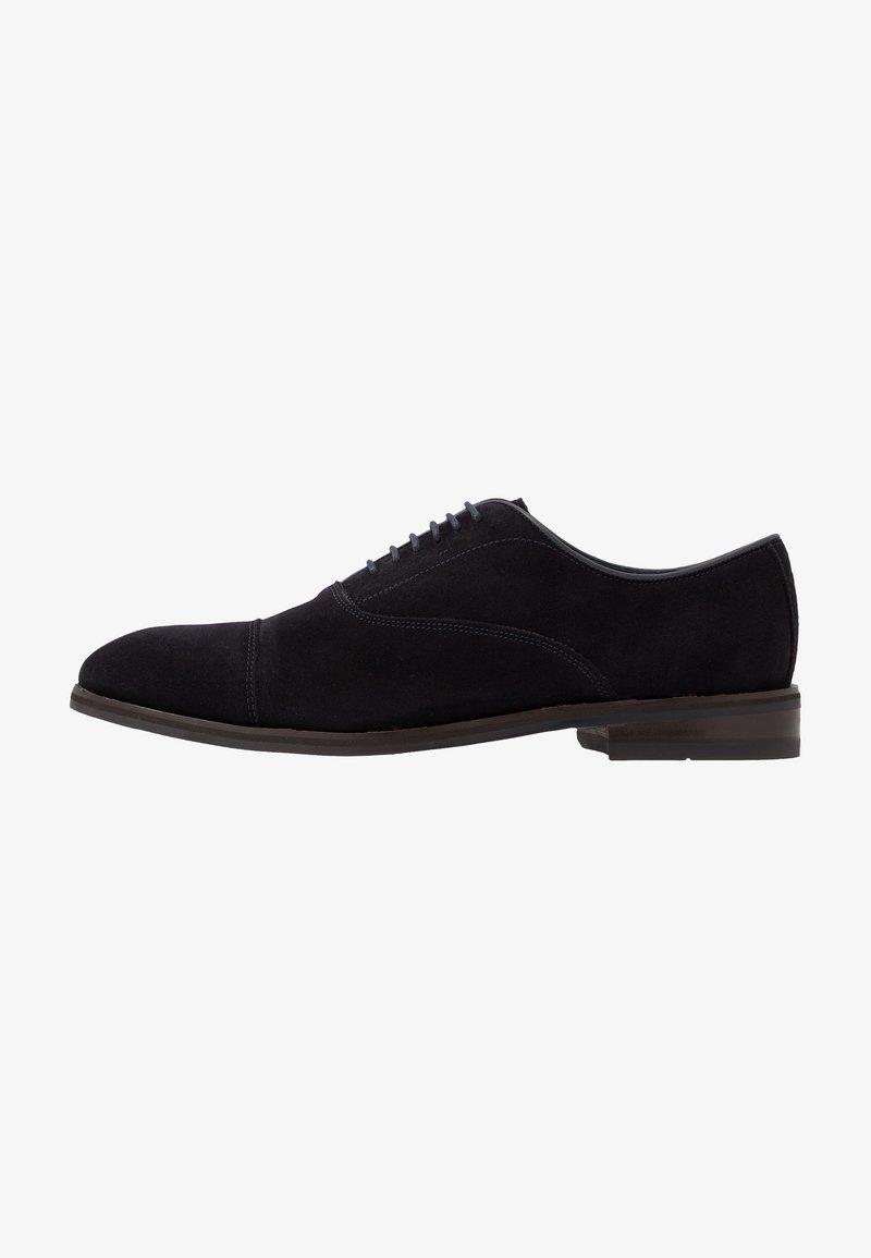 Chaussure Oxford pour homme en daim noir avec laçage fermé, design à bout droit et petit talon superposé, présentée en profil sur fond blanc.