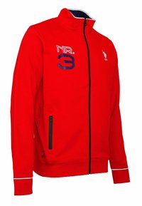 Röd zip-up hoodie med hög krage, marinblå detaljer och logotyp på vänster bröst. Har två framfickor med dragkedja och kontrasterande muddar.