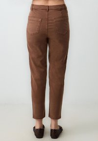 Pantaloni marroni a vita alta con gamba dritta, dotati di due tasche posteriori e una texture liscia e opaca. I pantaloni si restringono alla caviglia.