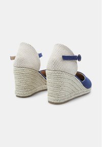 Plavi i bež espadrile s potpeticom od jute i remenom oko gležnja. Imaju okrugli vrh i otvorene strane za prozračnost.