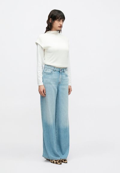 Ελαφρύ λευκό τοπ με κοντά μανίκια, συνδυασμένο με τζιν παντελόνι με φαρδιά μπατζάκια και ξεθωριασμένο μπλε χρώμα. Τα παπούτσια έχουν σχέδιο με λεοπάρ.