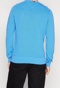 Maglione blu lavorato a maglia con maniche lunghe, texture a coste e scollatura rotonda. Presenta un dettaglio a righe sul collo della schiena.