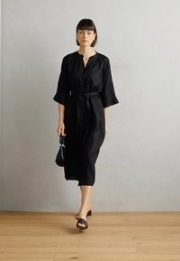 Μαύρο λινό φόρεμα πουκάμισο με κουμπιά, τρία τέταρτα μανίκια και αντίστοιχο ζωνάκι. Συνδυασμένο με μια μικρή μαύρη τσάντα και σανδάλια.